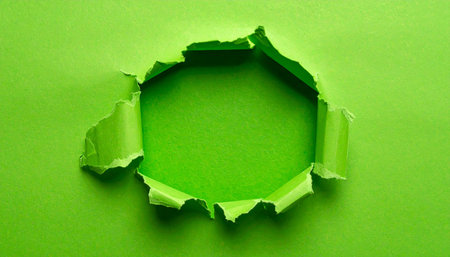 A jagged hole is torn in bright green paper, revealing a darker green surface within.の素材