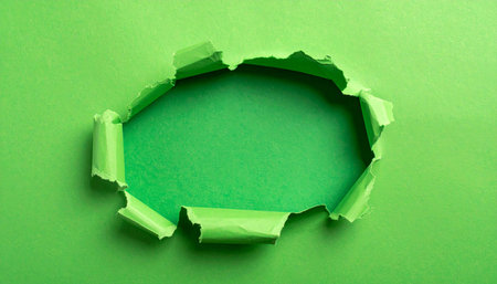 A jaggedly torn opening in vibrant green paper exposes a darker green surface with rough edges.の素材