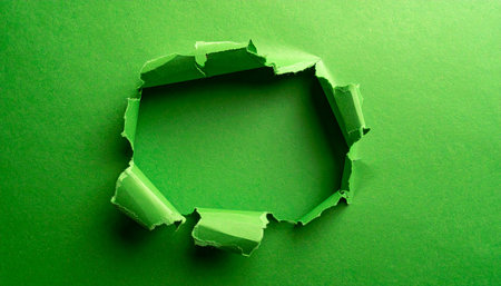An irregularly shaped hole is torn in bright green paper, exposing a darker green surface within.の素材