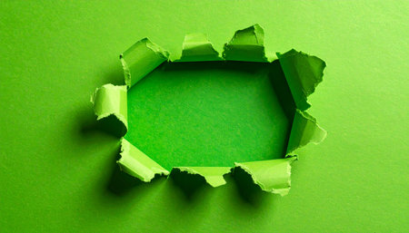 A jagged hole torn in bright green paper reveals a lighter green surface beneath. Clear details and vibrant colors en...の素材