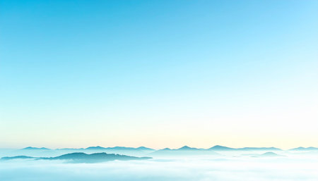 Horizon showing expansive misty mountain range under a clear bright blue sky with a faint white horizon glow.の素材