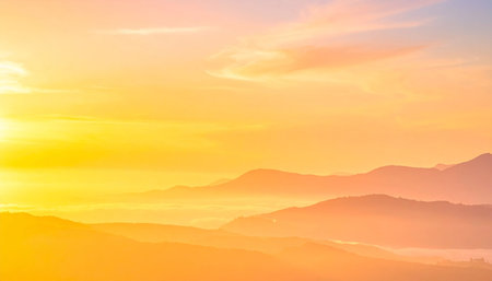 Gradient showing golden sunrise over misty mountain ranges with soft orange and pink sky and layered peaks.の素材