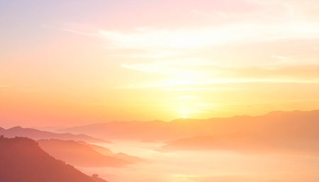 Soft pastel hues of pink and gold fill the sky over layered mountain ranges partially obscured by a gentle morning mist.の素材