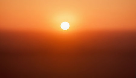 A bright white sun is centered in a warm gradient of orange and red, suggesting a strong sunrise or sunset.の素材