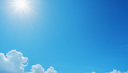 Clouds showing bright sun with prominent rays shines in a clear blue sky with fluffy white cumulus clouds in the...の素材