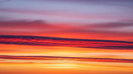 A dramatic sky filled with vibrant streaks of red, orange, and yellow clouds creates a natural spectacle at dawn or...の素材