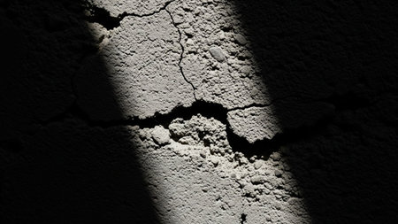 A close-up view of a cracked grey concrete surface with a stark diagonal shadow creating a dramatic abstract pattern.の素材