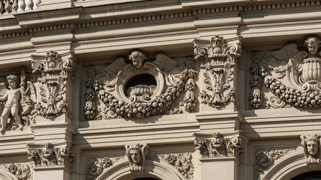 Close-up of a sunlit stone architectural facade featuring intricate carvings of cherubs, fruit garlands, and...の素材