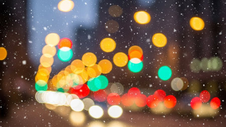 Soft focus bokeh lights of city traffic and falling snow at night creating a magical winter atmosphere.の素材