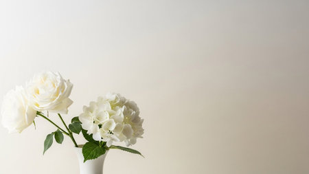 Delicate white roses and a hydrangea bloom are arranged in a simple white vase against a soft,...