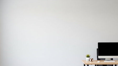 A minimalist desk with a computer, potted plant, and small jars sits against a plain white wall, offering ample copy...の素材