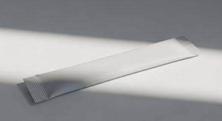 Dramatic showing white stick sachet or packet lying on a white surface with dramatic shadows and light.の素材