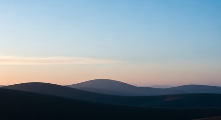 Gentle, rolling desert dunes create soft, flowing lines against a gradient pastel sky. The sky transitions from a pale blue at the to soft pinks and oranges near the horizon, suggesting either dawn or dusk. The dunes are rendered in deep, dark tones in the foreground, gradually lightening towards the background. The scene is characterized by its minimalist aesthetic, emphasizing the smooth forms of the landscape and the subtle interplay of light and color.の素材