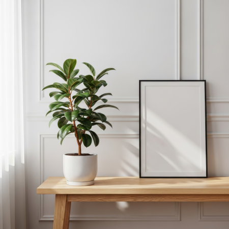 A healthy green plant in a white pot and an empty picture frame are displayed on a wooden table, presenting a clean aesthetic isolated on white background.の素材