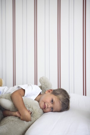 5 years old kid laying on his bed with stripped wallpaper on the backの写真素材