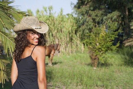 Young latin looking girl at countryside nearby a horse, looking backの写真素材