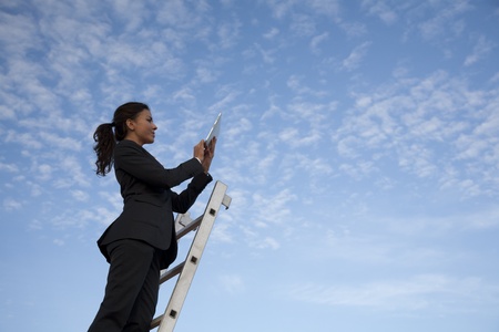 Young latin looking business woman, working with her iPad on a roof, with the blue sky in the background.の写真素材