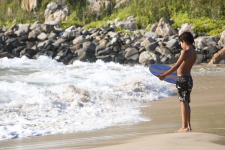 Kid with his wake board waiting for the wave at the beach.の写真素材