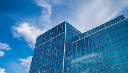 Reflection in windows of modern office building against blue sky with cloudsの素材