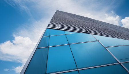 Low angle view of modern office building with blue sky and white cloudsの素材