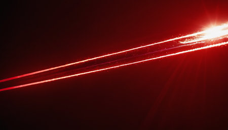 Red laser beam on a dark background. The rays of the sun are visible through the clouds.の素材