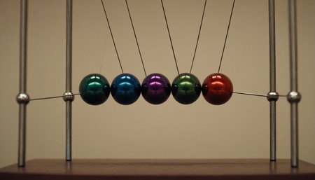 Newton's cradle with colorful balls on a wooden table, close upの素材