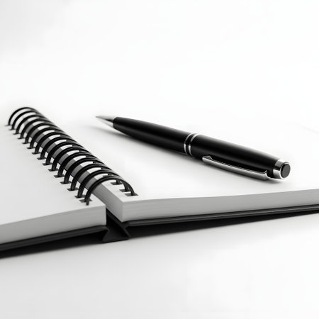 A black ballpoint pen lies on the blank page of an open spiral-bound notebook, ready for writing.の素材