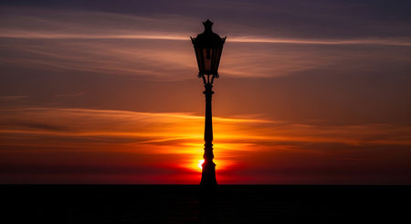 A classic lamppost stands as a stark silhouette against a dramatic sky painted with fiery oranges and deep purples during sunset.の素材