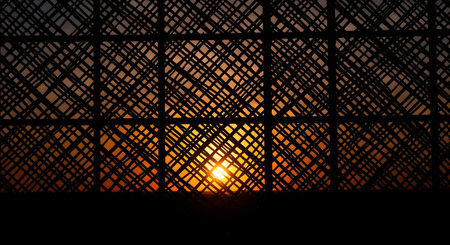 A warm sunset glows through a dark, crisscrossed bamboo lattice, creating a textured and atmospheric view.の素材