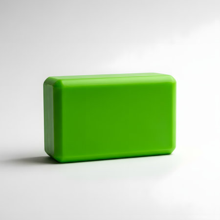 A vibrant, solid green bar of soap with rounded edges sits on a clean white surface, casting a subtle shadow.の素材