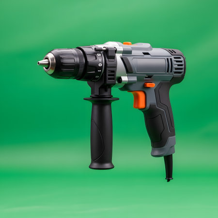 A black and silver cordless power drill with an orange trigger and auxiliary handle is shown against a solid green backdrop.の素材