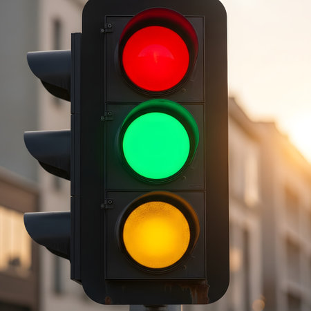 A close-up view of a vertical traffic light showing red green and yellow lights illuminated against a blurred urban background.の素材