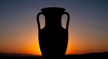 A dark silhouette of an ancient amphora stands tall against a dramatic sunset, with hues of orange, purple, and blue filling the sky.の素材