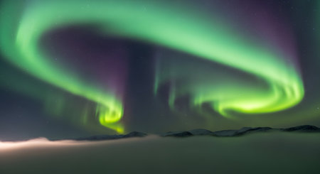 Spectacular display of the Northern Lights with swirling green and purple hues illuminating the dark, starry sky above a silhouetted landscape.の素材