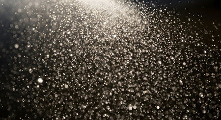 A close-up, abstract view of water droplets falling, illuminated by a bright light source creating a shimmering effect.の素材