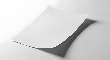 A clean, blank white sheet of paper is angled, casting a subtle shadow on a seamless white surface.の素材
