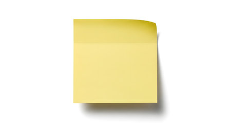 A close-up, top-down view of a single, empty yellow sticky note with a slightly curled and torn top right corner, casting a subtle shadow.の素材
