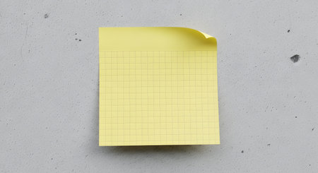 A single yellow sticky note with subtle grid markings is placed on a grey, speckled, textured background.の素材