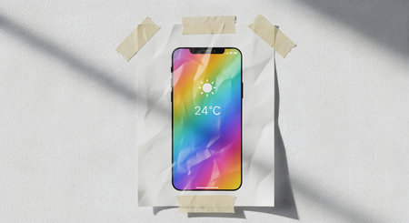 A sleek smartphone is taped to a textured surface, showcasing a colorful rainbow gradient on its screen. Shadows add depth to the scene.の素材