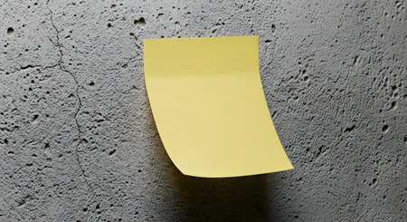 A single yellow sticky note is affixed to a rough, grey concrete surface, casting a subtle shadow.の素材