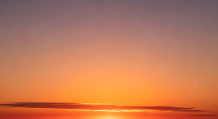 A warm, gradient sky transitions from deep orange to soft purple, with a thin band of clouds silhouetted against the bright horizon.の素材