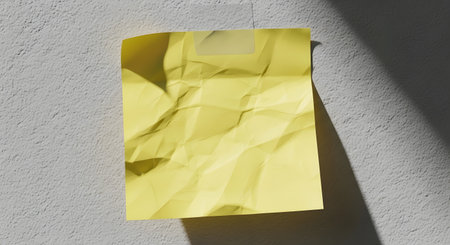 A single sheet of crumpled yellow paper lies on a textured gray surface, casting long, dramatic shadows from a light source above.の素材