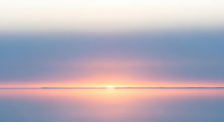 A tranquil ocean horizon at sunrise, with the sun's warm glow reflecting on the calm water and a soft pastel sky above.の素材