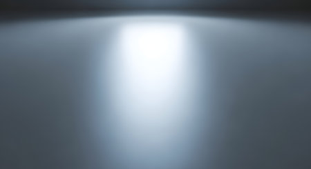 A strong, bright beam of light emanates from above, illuminating a textured, gray surface with a subtle grid pattern.の素材