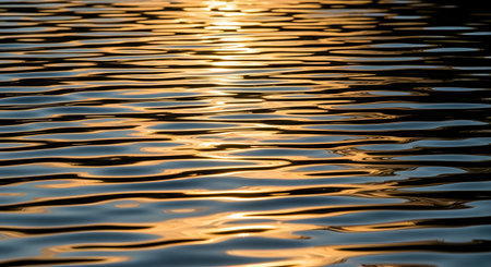 Close-up view of shimmering water with golden light reflecting off its textured surface, creating abstract patterns.の素材