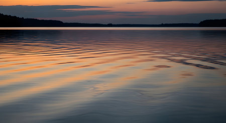 The warm hues of a sunset paint the sky and cast vibrant reflections on the gently rippling surface of a calm body of water.の素材