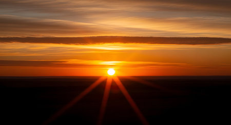 A breathtaking sunset paints the sky with fiery oranges and yellows, the sun a bright orb casting dramatic rays over a dark landscape.の素材