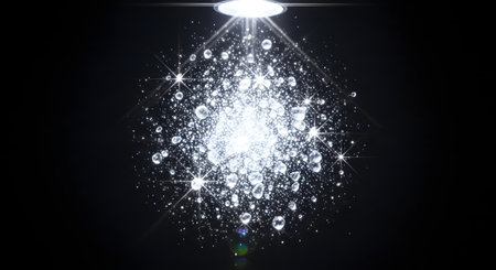 A close-up view of a shower head emitting a bright light, illuminating a cascade of sparkling water droplets against a dark background.の素材