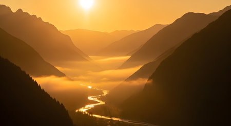 A breathtaking sunrise bathes a serene mountain valley in warm golden light, with mist swirling around a winding river below.の素材