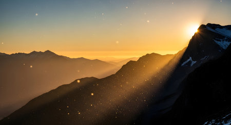 A breathtaking sunrise casts golden light and dramatic rays across a rugged mountain range, highlighting snow-capped peaks and misty valleys.の素材